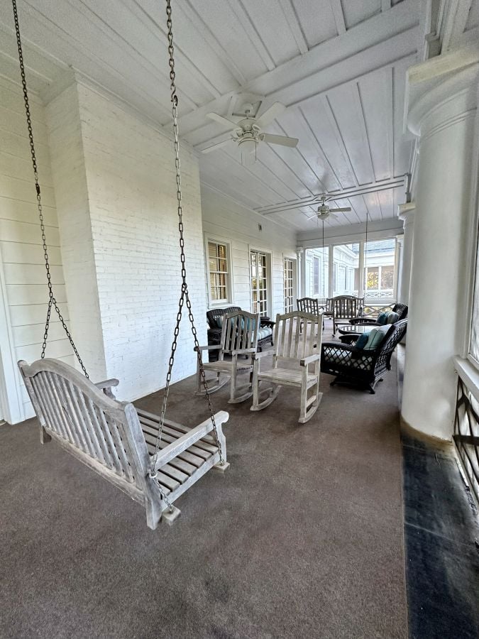 The second floor porch attached to the second floor rooms, with a swing and sitting areas, screened in, at the Duke Mansion, one of the historic hotels in Charlotte.