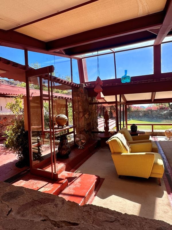 Bright indoor lounge with yellow chairs and large glass windows showing outdoor garden in the living room at Taliesen West, in Scottsdale, Arizona.